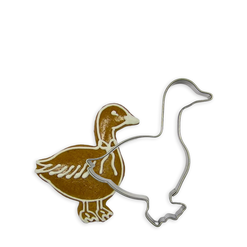 Goldene Gans als Plätzchen verziert neben der weißen Kontur einer weiteren Gans welche eine Ausstechform aus Metall ist