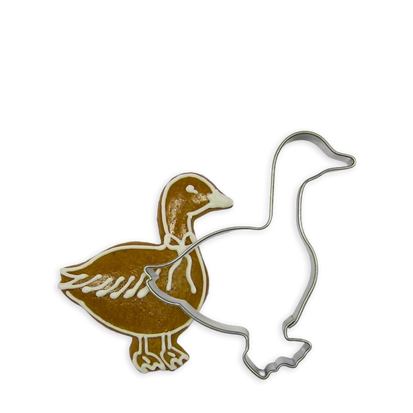 Goldene Gans als Plätzchen verziert neben der weißen Kontur einer weiteren Gans welche eine Ausstechform aus Metall ist