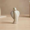 Graue, minimalistische Handschmeichler Statue in Form eines Engels steht auf einem Tisch aus Holz