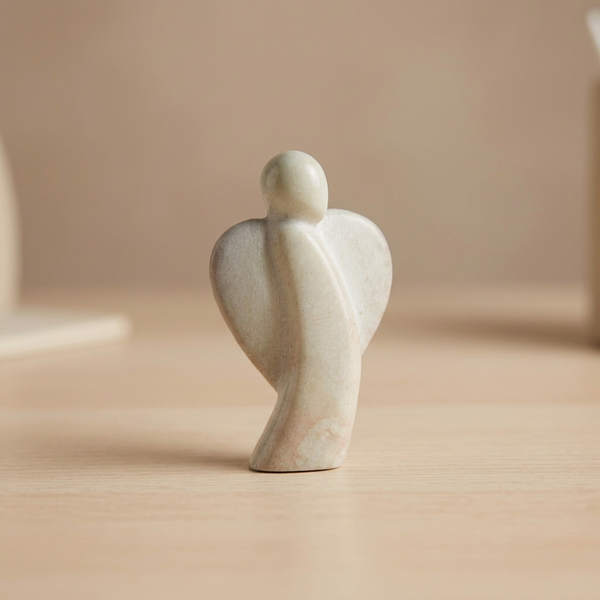 Graue, minimalistische Handschmeichler Statue in Form eines Engels steht auf einem Tisch aus Holz